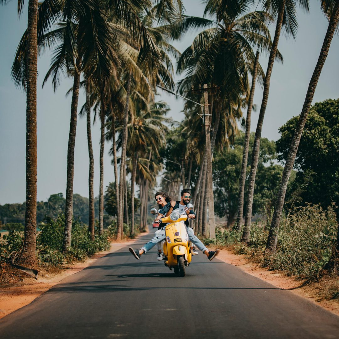 pexels-photo-2174656-2174656 A joyful couple rides a yellow scooter through a scenic palm-lined road, capturing the essence of tropical travel and adventure.